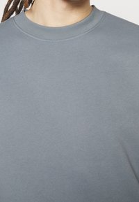 Sweatshirt en coton gris à col rond avec une texture lisse et un col en côtes. Design simple, sans motifs ni accents.