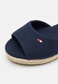 Granatowe tkaninowe sandały na płaskiej podeszwie z otwartym przodem, z plecioną podeszwą z juty i z małym detalem w kolorze czerwonym, białym i niebieskim.