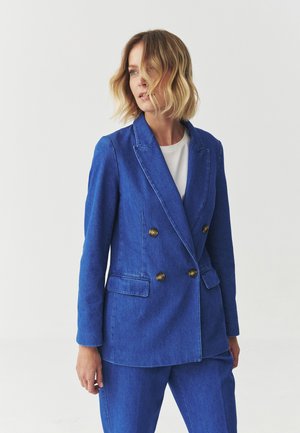 Blazer de denim azul con diseño de doble botonadura, botones dorados y solapas con muesca. Presenta bolsillos laterales y un ajuste entallado.
