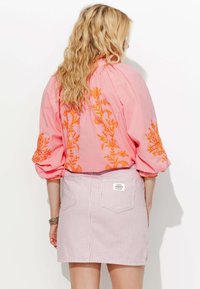 Blouse rose avec broderie florale orange dans le dos et sur les manches, associée à une jupe en denim rayée avec deux poches arrière et une étiquette.