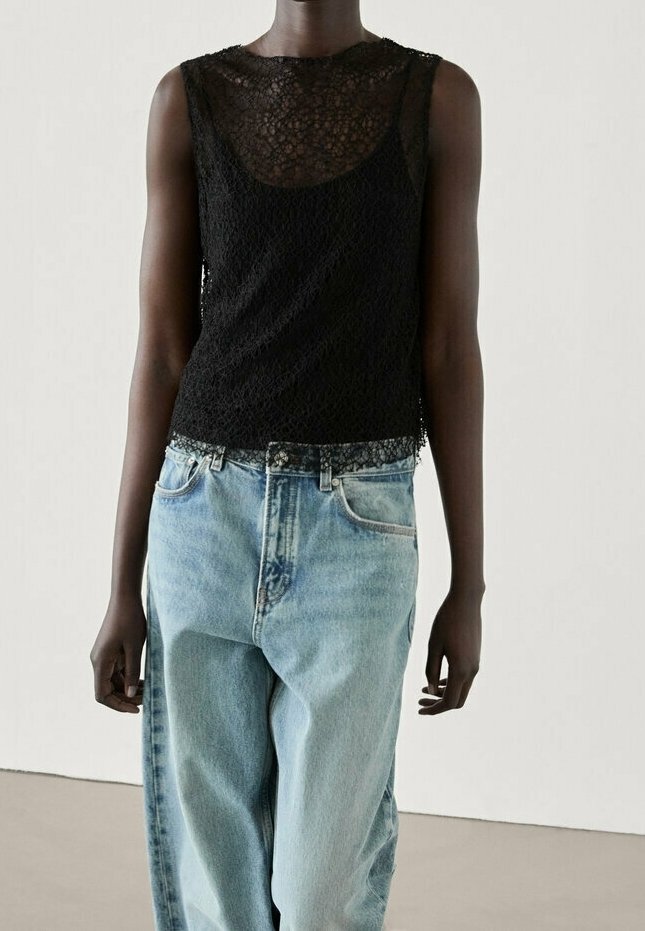Haut en dentelle sans manches noir avec un col rond, associé à un jean en denim léger et ample avec un design classique à cinq poches.
