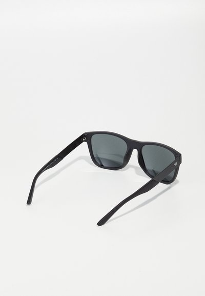 Ochelari de soare negri cu lentile rechteunghiulare, finisaj mate, brațe subțiri și un detaliu cu logo pe o parte. Lentilele fumurii gri oferă protecție UV.