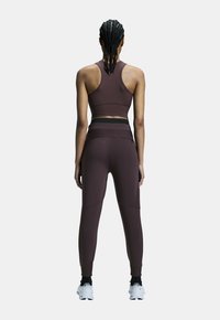 Burgundské športové crop top a legíny. Obsahuje bezšvový dizajn, pretečený chrbát a zúžené nohavice s členkovými manžetami, vyrobené z elastického materiálu.