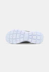Semelle d'une chaussure de sport noire et blanche montrant un motif de bande de roulement blanche avec des rainures de flexion et des zones d'adhérence texturées.