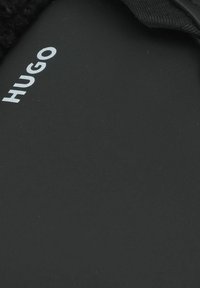 Infradito neri con cinturino in tessuto testurizzato e suola opaca nera. Presenta il logo "HUGO" in un carattere sans-serif moderno di colore bianco.