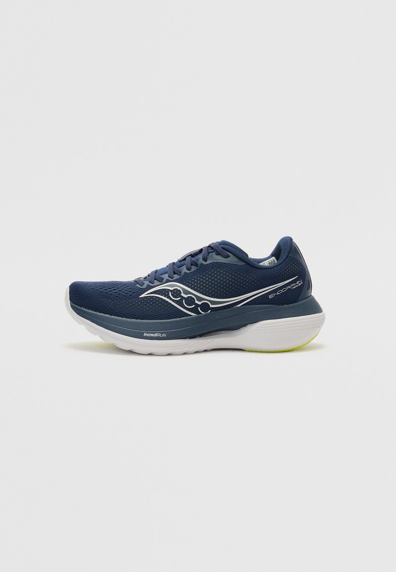 Zapatilla de running de color marino con parte superior de malla, acentos blancos y suela gruesa con detalles en verde. El diseño incluye un logo en el lateral y cordones.