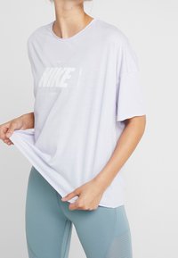 Camiseta Nike de color púrpura claro con mangas cortas y un logo blanco, combinada con leggins azul claro que presentan acentos texturizados.