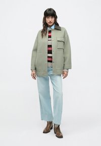 Svetlo zelena prevelika jakna z ovratnikom, s prsnim žepom. Nošena preko večbarvnega puloverja s črtami in svetlo modrih kavbojk. Rjavi škornji.