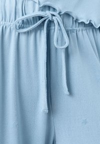 Lyseblåt tekstureret stof med snøre i taljen, prydet med en flæsekant og diskrete stjernemønstre på stoffet.