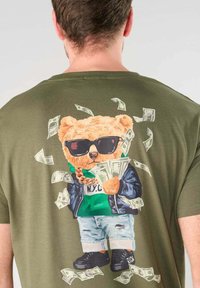 Camiseta con un gráfico de un oso que lleva gafas de sol, una cadena, una chaqueta y zapatillas, sosteniendo dinero con billetes flotando alrededor.