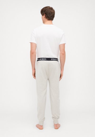 Biała koszulka z krótkim rękawem, w zestawie z jasnoszarymi spodniami dresowymi z czarnym pasem, na którym widnieje tekst "POLO RALPH LAUREN".