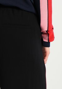 Czarne spodnie o gładkiej fakturze z tylną kieszenią, w połączeniu z wielokolorowym swetrem z przędzy, w czerwone, różowe i granatowe paski.