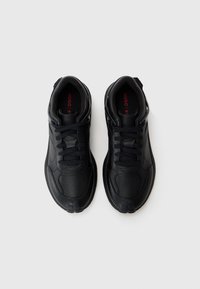 Black athletic shoes with textured synthetic material, round toe, lace-up design, and prominent logo detail with a red accent inside.