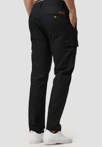 Black cargo pants featuring side pockets, a back pocket with button closure, and a leather accent on the waistband. Paired with white sneakers.