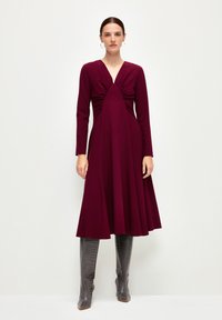 Burgundin mekko pitkillä hihoilla, kerätty yläosa ja levenevä helma. Yhdistetty kiiltäviin, polvenkorkuisiin harmaisiin krokotiilinahkakuosisiiin saappaisiin.