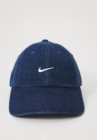 Denim kapa v temno modri barvi s ukrivljenim robom. Na sprednji strani je izvezen bel Nike logotip. Mehka tekstura in konstrukcija s šestimi paneli.