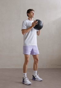 Witte korte mouwen shirt, licht paarse shorts, zwarte basketbal, witte sokken en zwart-paarse sneakers, voor een neutrale muur.