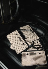 Vijf gestikte handtassen van beige stof met zwart accent, elk met een ritssluiting en metalen studs, zijn op een zwart leren stoel gestapeld.