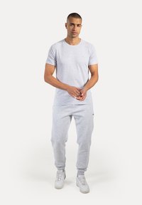 Lichtgrijze crewneck t-shirt gecombineerd met bijpassende sweatpants. Beide kledingstukken hebben een gladde textuur en minimale branding. Witte sneakers maken de look compleet.