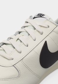 Κοντινό πλάνο σε λευκό δερμάτινο αθλητικό παπούτσι Nike με λευκά κορδόνια και μαύρο λογότυπο Nike στη πλευρά.