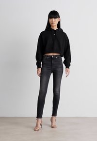 Black cropped hoodie with a drawstring, paired with dark skinny jeans and beige heeled sandals. Simple design with a smooth texture.
