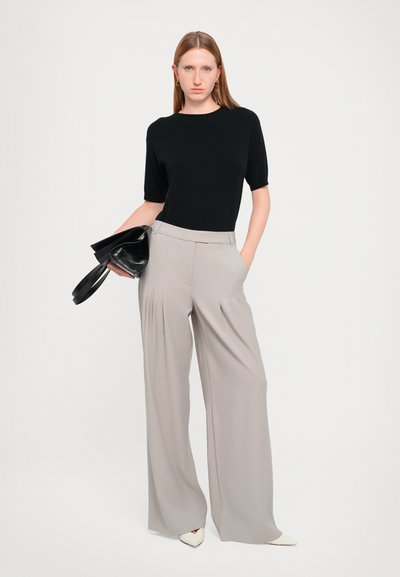 Zwarte shirt met korte mouwen en ronde hals, gecombineerd met lichtgrijze wijde broek met voorplooien. Accessoires zijn een zwarte clutch.