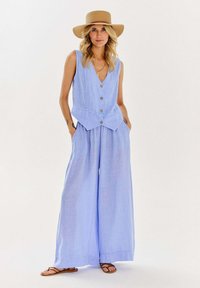 Svetlomodrý ľanový overal s priliehavým topom v štýle vesty, zapínaním na gombíky a širokými nohavicami. Hladká textúra s vreckami po stranách.