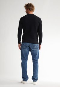 Black knit sweater with long sleeves, crew neckline, and textured fabric; paired with light blue denim jeans and white sneakers.