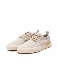 Zapatillas de lona beige con puntera redonda, diseño de cinco ojales con cordones, acento amarillo en el talón y suela de goma texturizada para mayor agarre.