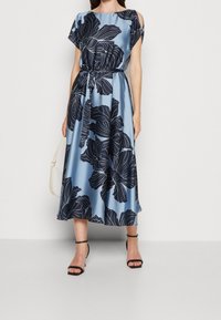 Robe en satin bleu avec de grands imprimés floraux marins, manches courtes et taille froncée. Présente un design fluide et une jupe longueur cheville.