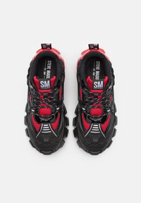 Schwarze und rote Sportschuhe mit einem Obermaterial aus Mesh, dicker Sohle und ausgeprägtem Profil. Enthält Markenakzente an der Zunge und der Ferse.