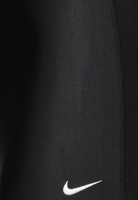 Svarte atletiske leggings laget av elastisk stoff, med en hvit Nike-logo og en glatt tekstur med forsterkede sidesømmer.