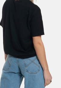 Svart kortärmad T-shirt med avslappnad passform, i kombination med ljusblå högmidjade jeans med synlig sömnad och fickor.