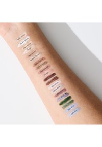 Swatches on a light brown arm showcasing various eyeshadow shades, including matte and pearly finishes, labeled with color names.