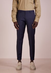 Marina tapered byxor med elastiska muddar, slätt tyg, sydda sömmar, bärs med en beige långärmad skjorta och ljusa sneakers.