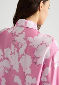 Roze bloemenblouse met een zachte, zijdeachtige textuur, uitgerust met grote witte en lichtroze bloemenpatronen en een klassiek overhemdkraagontwerp.