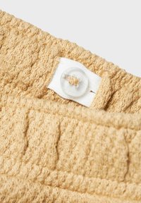 Tissu texturé beige avec un motif en boucle ; présente une fermeture à bouton blanc avec un bouton circulaire transparent et des détails de couture.