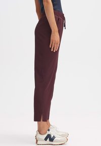 Bordeaux joggers met een elastische taille, trekkoord en zijsplitten aan de zoom, gecombineerd met witte sneakers met marineaccenten.