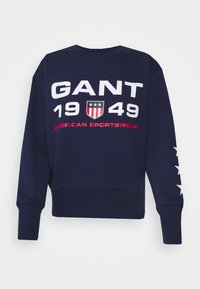 Námořnická modrá mikina z bavlny, s výrazným bílým a červeným textem: "GANT 1949 AMERICAN SPORTSWEAR" a hvězdami na rukávech.