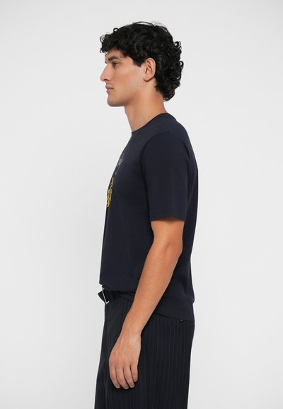 T-shirt navy in cotone con maniche corte e scollo a girocollo, caratterizzato da una stampa grafica sulla parte frontale. Texture liscia, abbinato a pantaloni a righe.