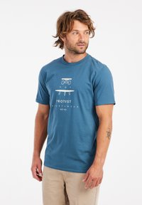 Mėlynas medvilninis marškinėliai trumpomis rankovėmis su baltu grafiku, vaizduojančiu riedlentę, ir tekstu "PROTEST SPORTSWEAR EST. 93" apačioje.