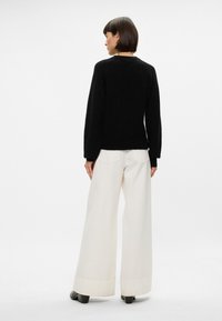 Black sweater with a crew neckline and long sleeves, paired with white wide-leg trousers, featuring a smooth fabric and subtle texture.