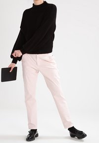 Svart överdimensionerad stickad tröja med hög krage, kombinerad med ljusrosa figurnära byxor. Svarta skor med detaljer. Håller i en svart kuvertväska.