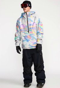 Veste de neige colorée avec motifs abstraits, en matériau léger, dotée d'une poche frontale et d'une capuche ajustable. Pantalon noir et gants.