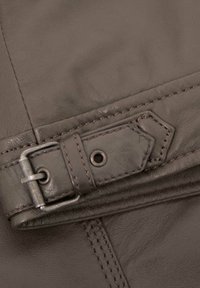 Brown leather strap with a metallic buckle and stitching details, featuring a textured surface and a snap closure on one end.