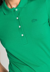 Polo shirt vert en coton texturé, avec un col, une patte de boutonnière à quatre boutons et un logo brodé sur la poitrine gauche.