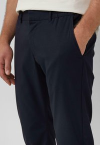 Marineblauwe chinos met een zachte textuur, voorzien van zijzakken en een relaxte tailleband voor comfort, gedeeltelijk getoond vanaf de taille naar beneden.