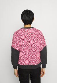 Sudadera de patrón rojo y blanco con un diseño geométrico, con mangas y dobladillo negros. Tejido suave con un ajuste relajado.