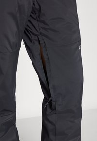 Pantalons isolés noirs avec une ouverture zippée sur le côté, texture lisse et coutures renforcées pour une durabilité optimale.
