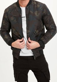 Black and green camouflage bomber jacket with ribbed cuffs and collar, zip closure, and lightweight, smooth fabric texture.